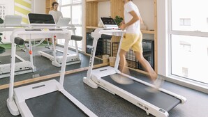 A gym with treadmills, a mirrored wall, and wooden shelves with exercise balls.