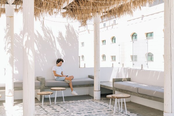 A person sitting on a white outdoor bench with a patterned floor and a thatched roof overhead. - Dara Al Yamamah Hotel (Jeddah)