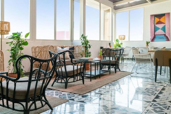 A spacious room with large windows, wicker furniture, and a tiled floor.