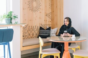 A modern interior with a round glass table, a wooden wall with geometric patterns, a blue chair, and a sofa with patterned cushions. - Dara Al Yamamah Hotel (Jeddah)