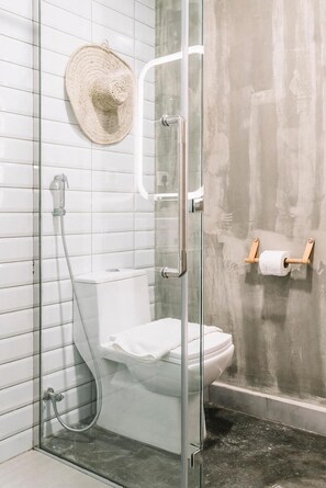 A modern bathroom with a glass-enclosed shower, white tiles, a toilet, and a straw hat on the wall. -  Dara Al Yamamah Hotel (Jeddah)