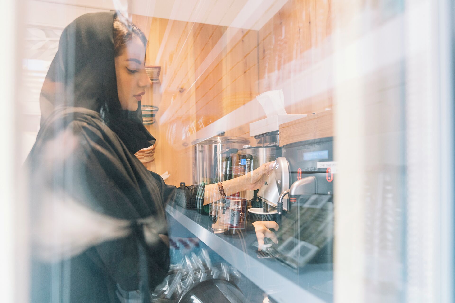 A person operating a coffee machine inside a cafe with wooden interior.