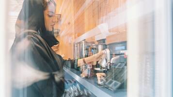 A person operating a coffee machine inside a cafe with wooden interior.