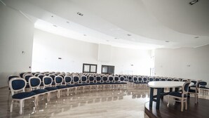 A conference room with rows of chairs and a central table, white walls, and a wooden floor. - Family Hotel (Polla)