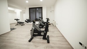 A modern gym with cardio machines, a bench, and a door in the background. - Family Hotel (Polla)