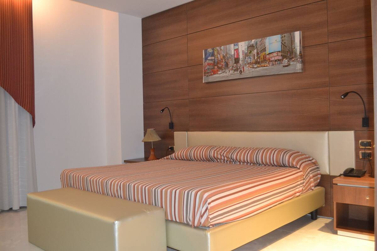 A hotel room with a bed, a bedside table, a lamp, and a painting on the wall.