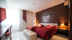 A hotel room with two beds, a desk, a chair, and a bench. - Family Hotel (Polla)