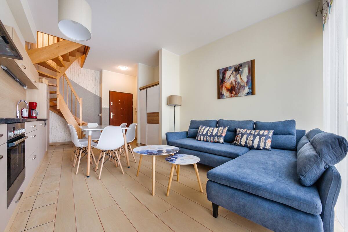 A modern living room with a blue sofa, a dining table with chairs, and a staircase leading to another level.