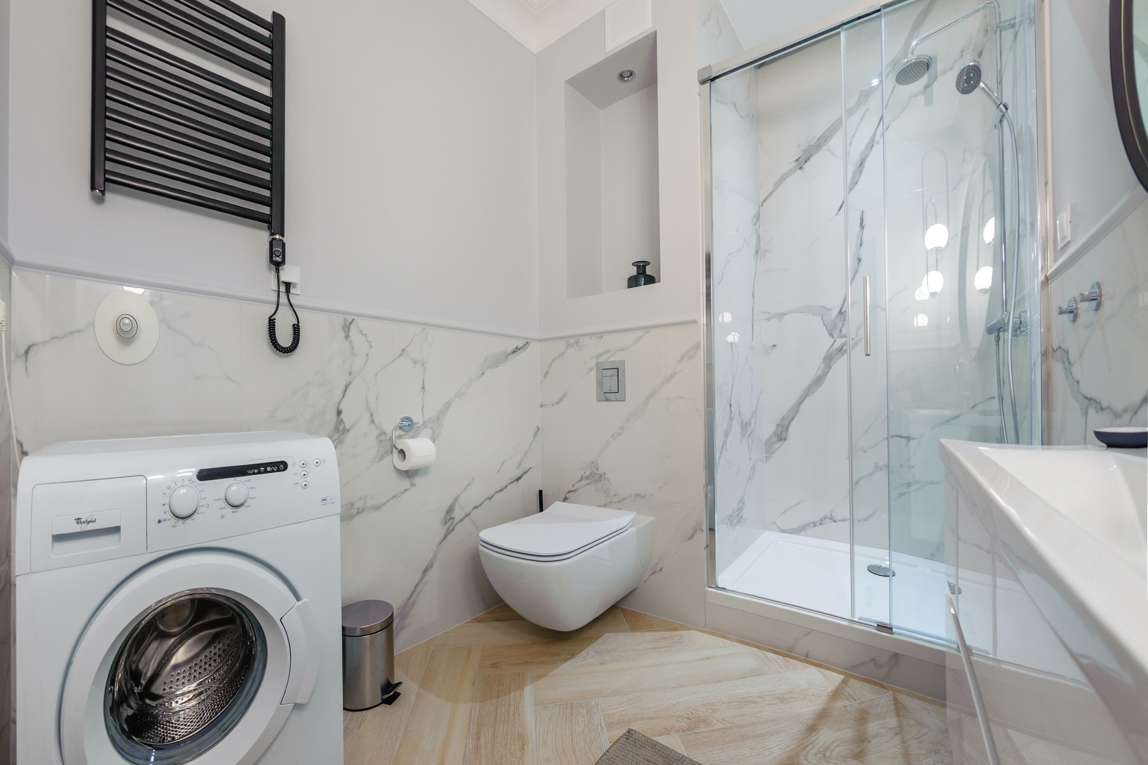 A modern bathroom with a built-in washer, toilet, and glass shower enclosure.