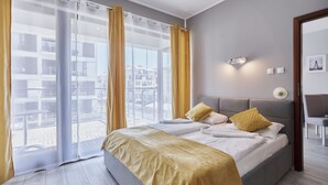 A modern hotel room with a large bed, a view of the city through floor-to-ceiling windows, and a balcony. - Apartamenty Sun & Snow Plaża (Swinoujscie)