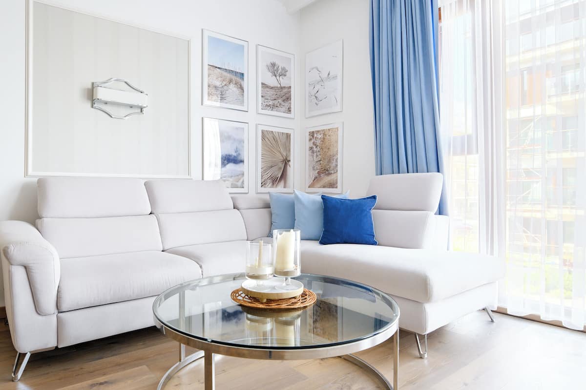 A modern living room with a white sofa, a glass coffee table, and artwork on the walls.