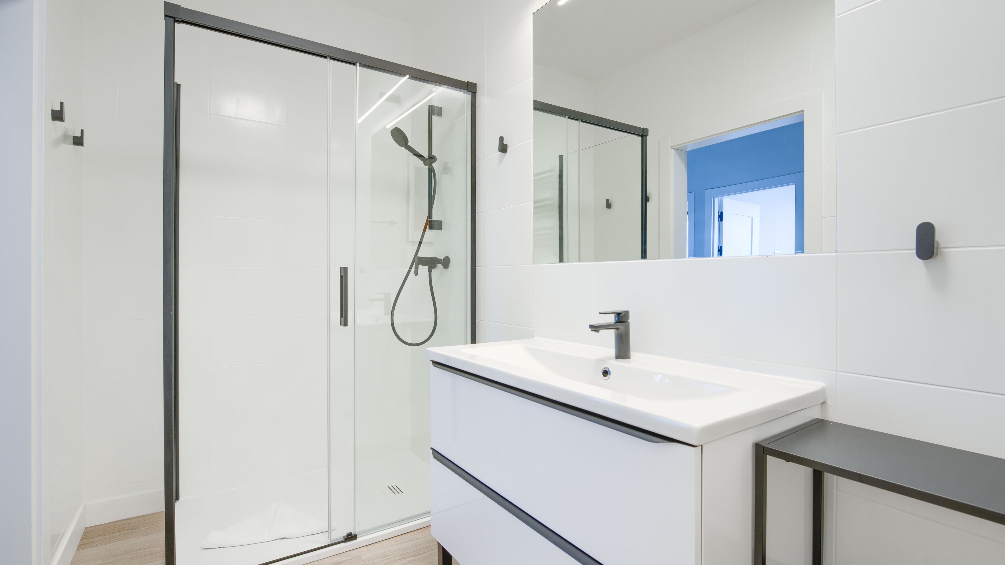 A modern bathroom with a glass shower enclosure, a white sink, and a large mirror.