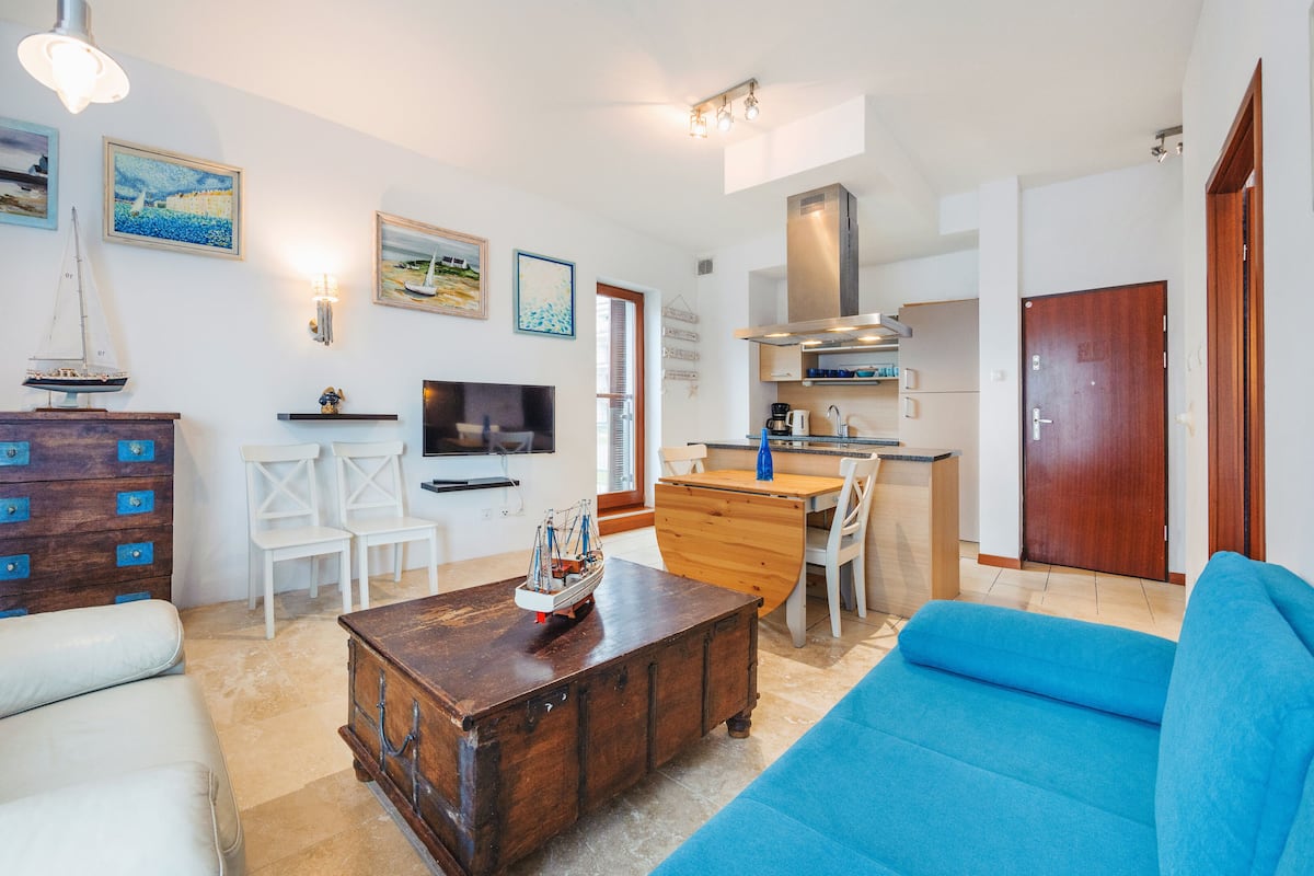 A living room with a sofa, a coffee table, a TV, a wooden cabinet, and a dining area with chairs and a table.
