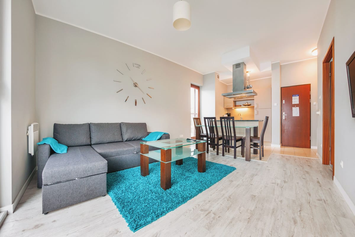 A modern living room with a grey sofa, a glass coffee table, and a blue rug.
