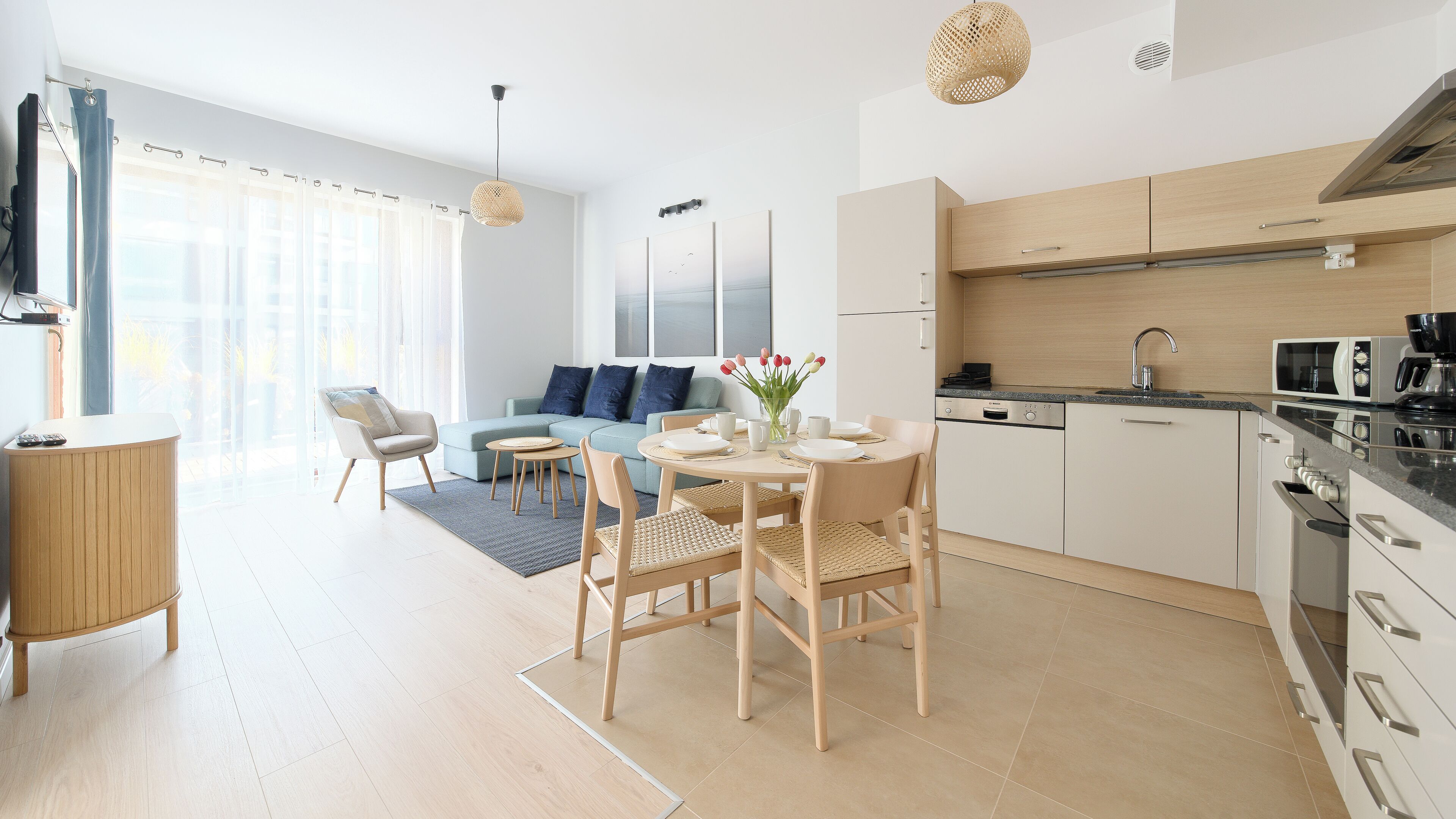 A modern kitchen with a dining area, a living room with a sofa, and a view of the outdoors.