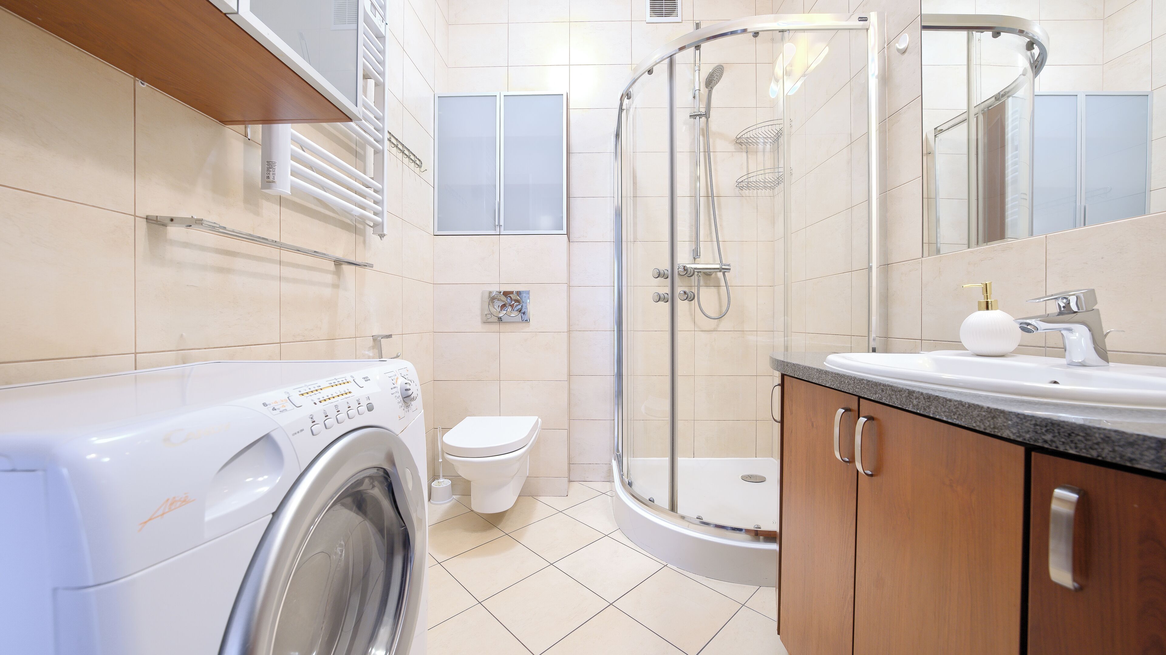 A modern bathroom with a washing machine, toilet, shower, and sink.