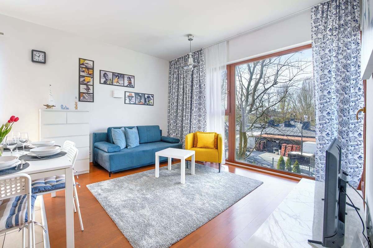 A modern living room with a blue sofa, a yellow armchair, and a dining area with a white table and chairs.