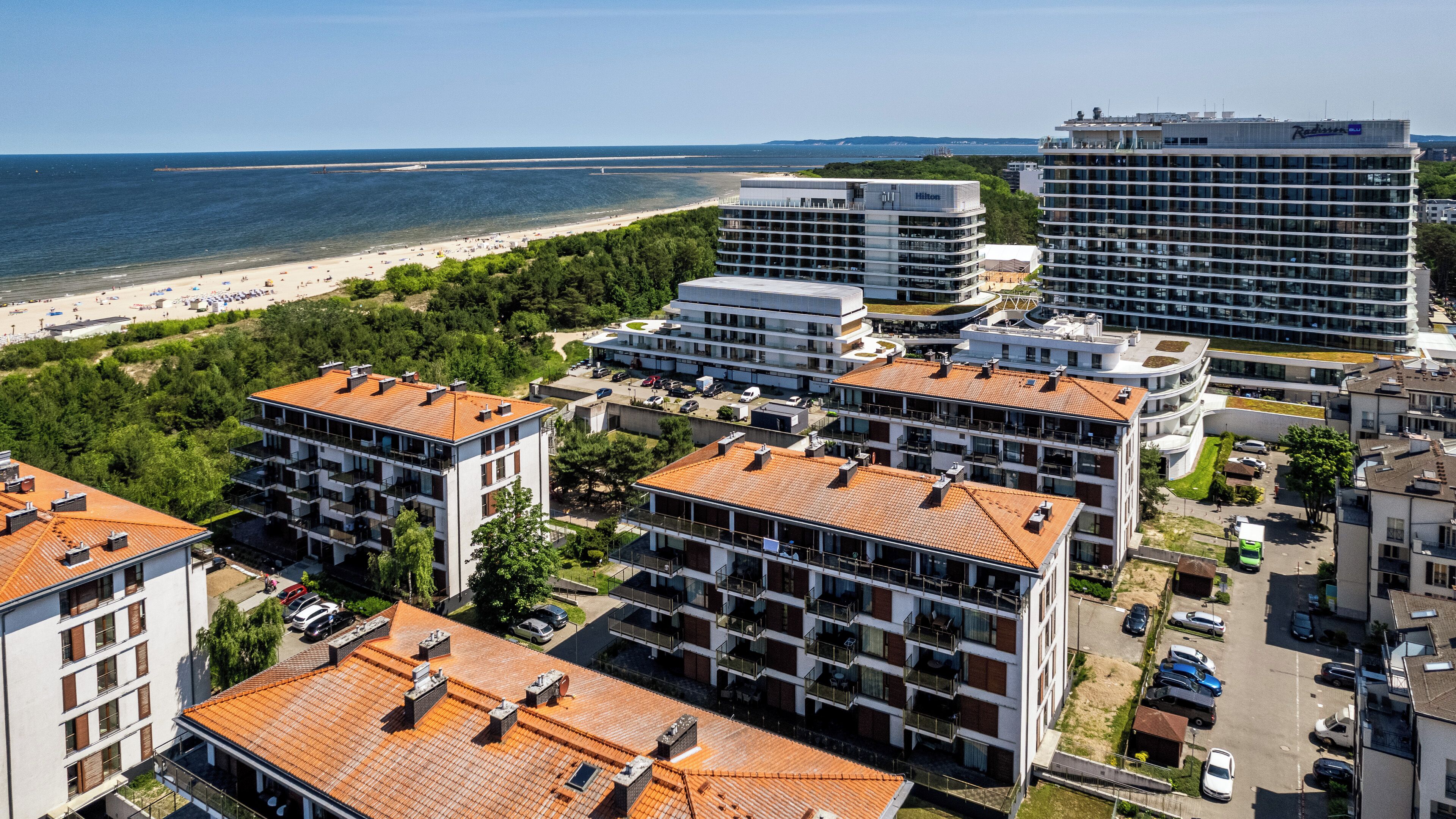 Zona costera hotelera con varios edificios, incluyendo un Hilton y un Radisson Blu, con vistas a una playa y una vista despejada del mar.
