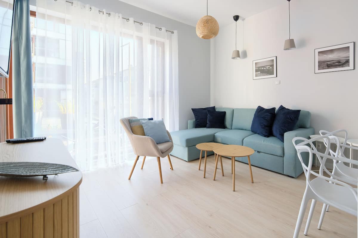 A modern living room with a light blue sofa, a wooden coffee table, and a white dining area.