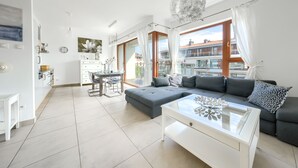 A modern living room with a grey sofa, a glass coffee table, and a dining area with a white table and chairs. - Apartamenty Sun & Snow Plaża (Swinoujscie)