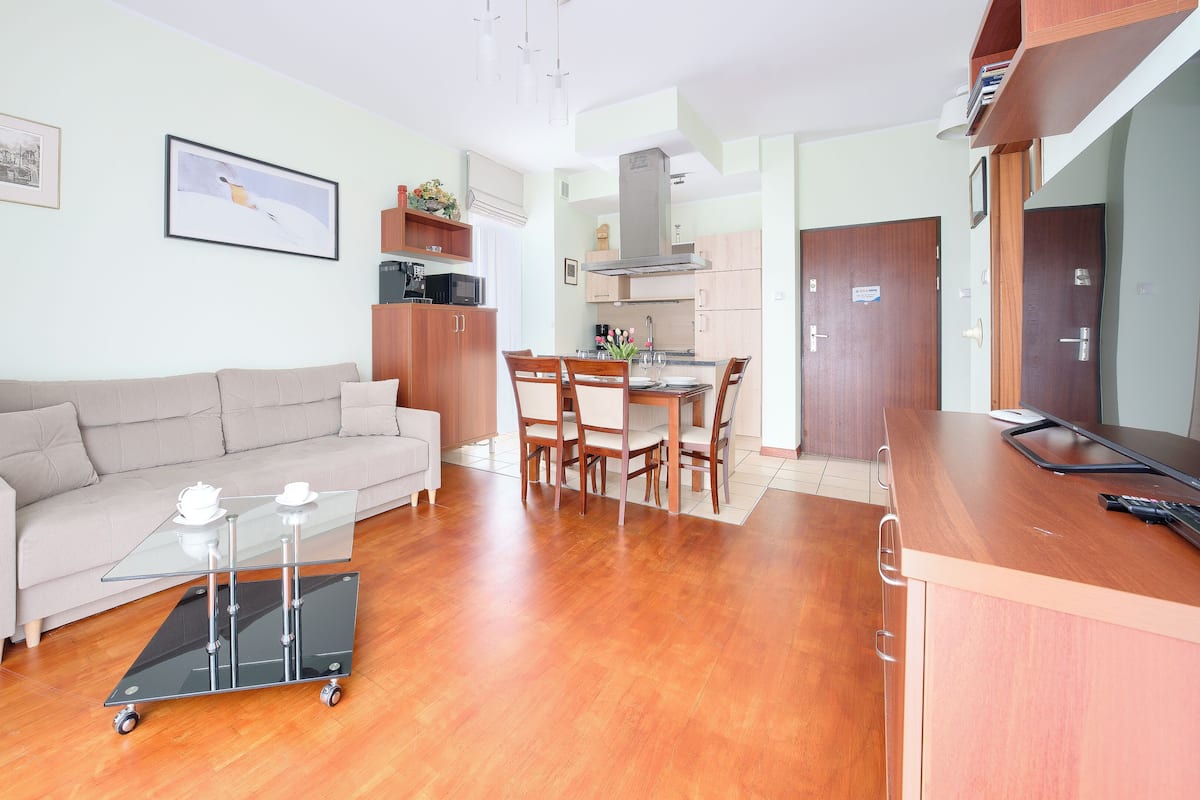 A modern living room with a sofa, a glass coffee table, and a dining area with chairs and a table.