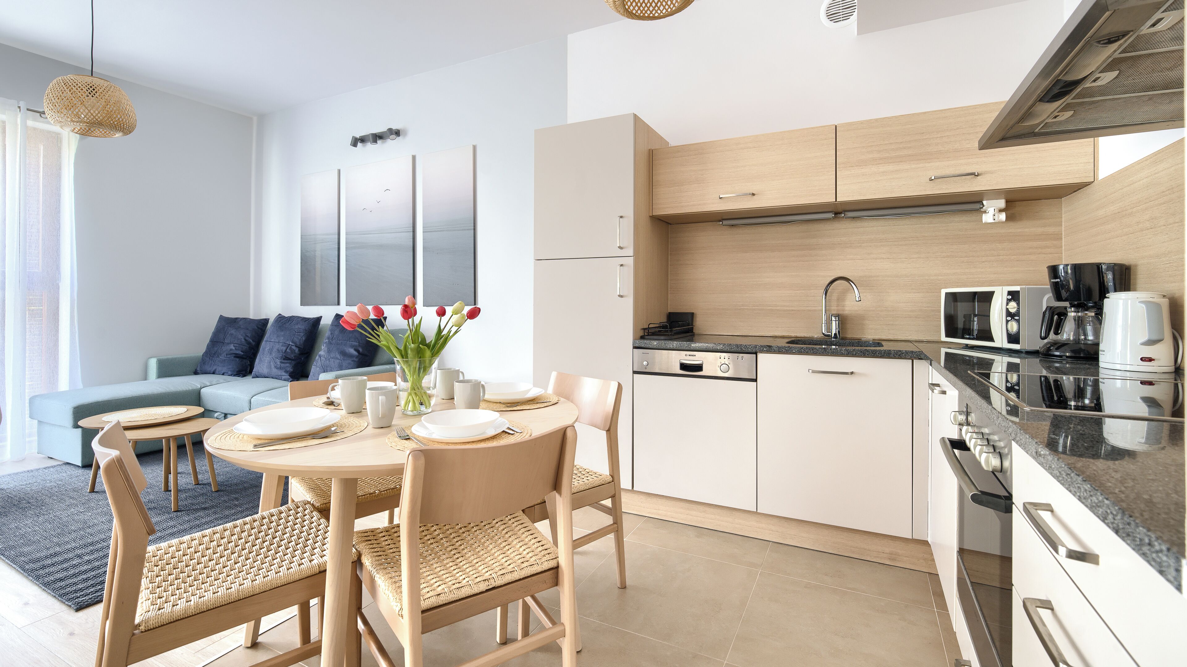 A modern kitchen with a dining area, featuring a round table, chairs, and a vase with flowers.