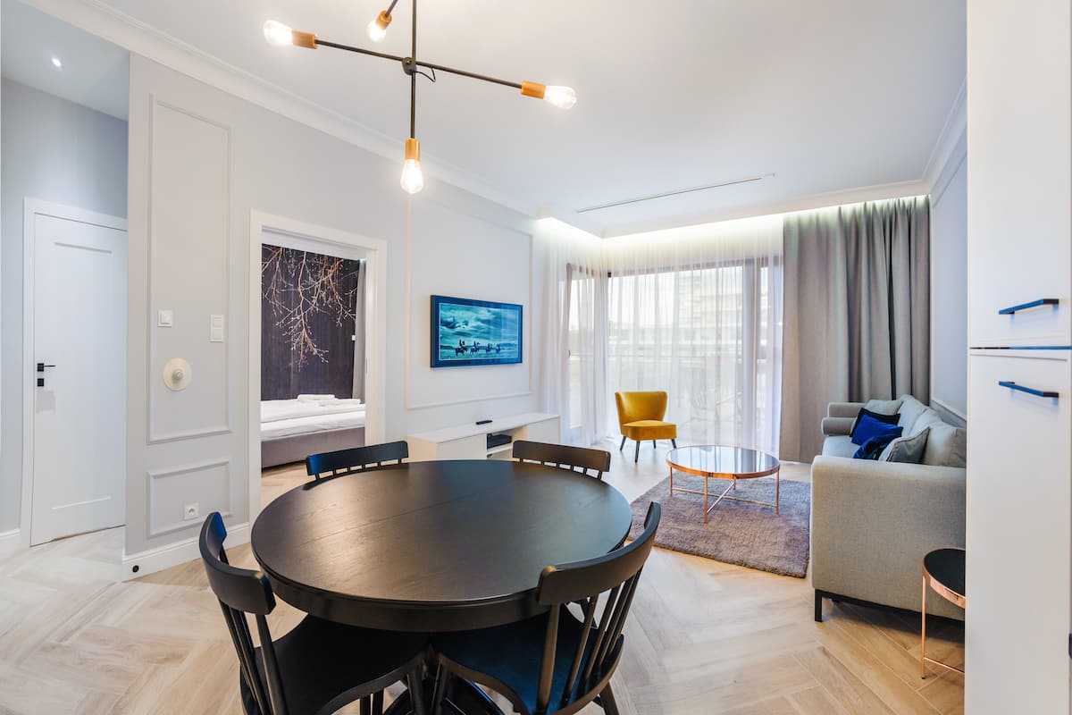 A modern living room with a round dining table, a sofa, and a TV mounted on the wall.