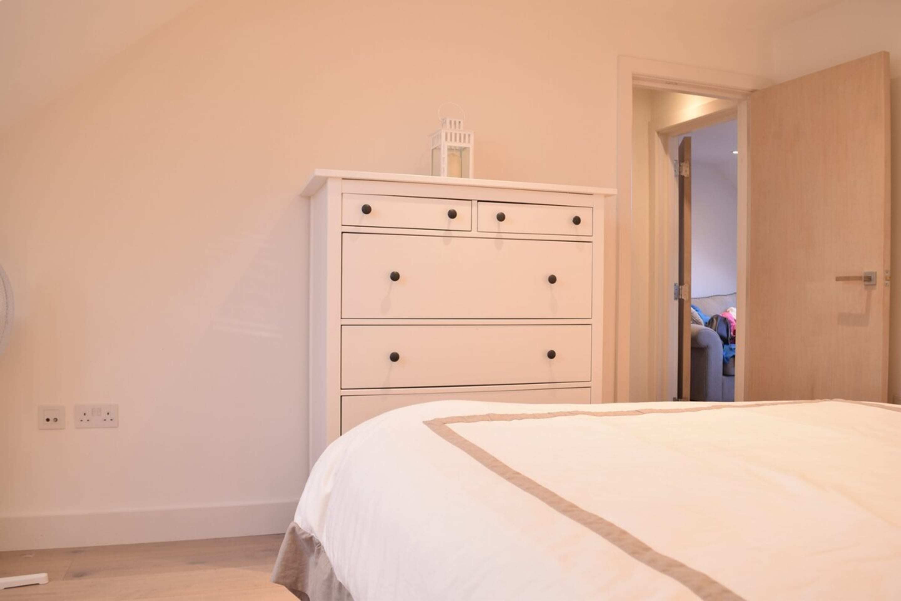 A bedroom with a bed, a white dresser with drawers, and a door leading to another room.