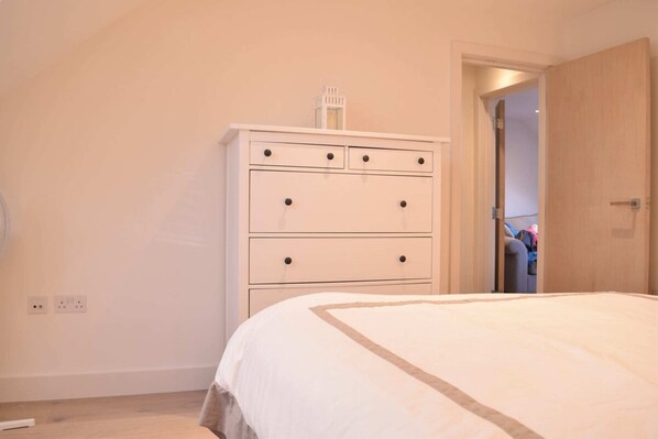 A bedroom with a bed, a white dresser with drawers, and a door leading to another room.