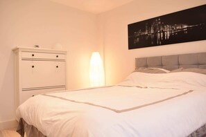 A bedroom with a bed, a nightstand, a lamp, and a cityscape painting on the wall.