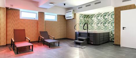 A modern room with a wooden slatted wall, a seating area with a bench and chairs, a hot tub, and a door with a patterned wallpaper.