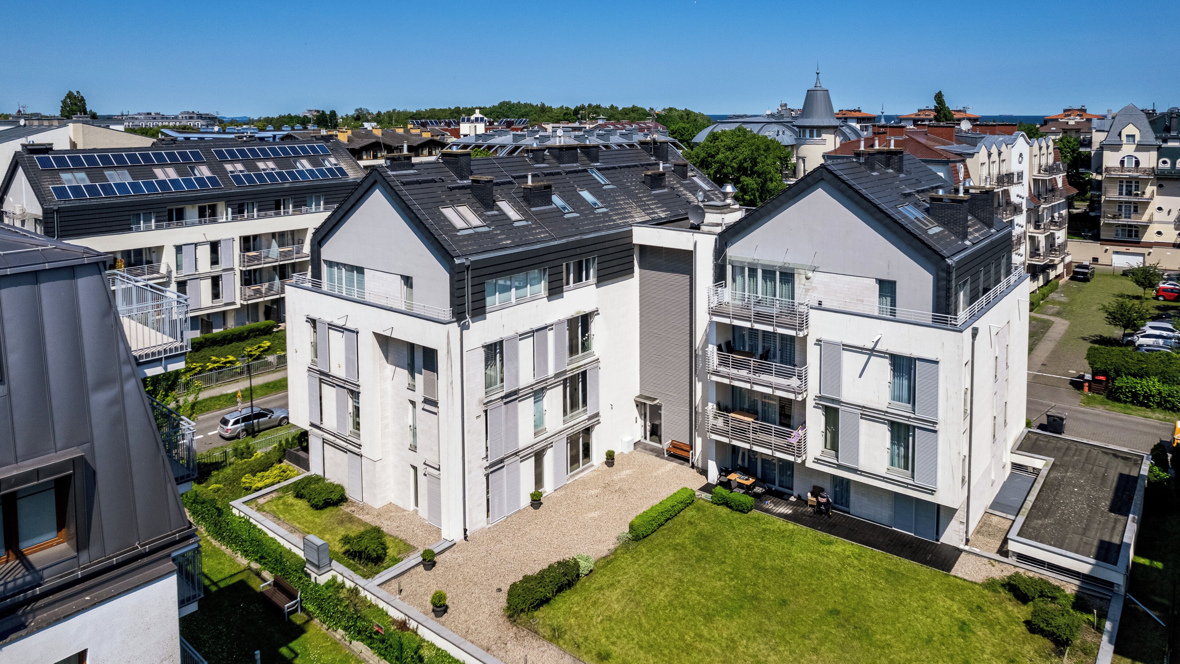 Un immeuble d’appartements moderne doté de nombreux balcons, de panneaux solaires sur le toit et d’un espace jardin bien entretenu.