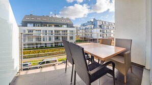 A balcony with a table and chairs, overlooking a residential area with modern buildings and a clear sky.