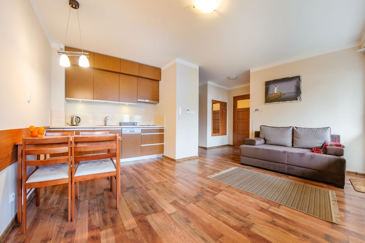 Une cuisine moderne avec des meubles en bois, une table à manger avec des chaises et un coin salon comprenant un canapé et un tapis.