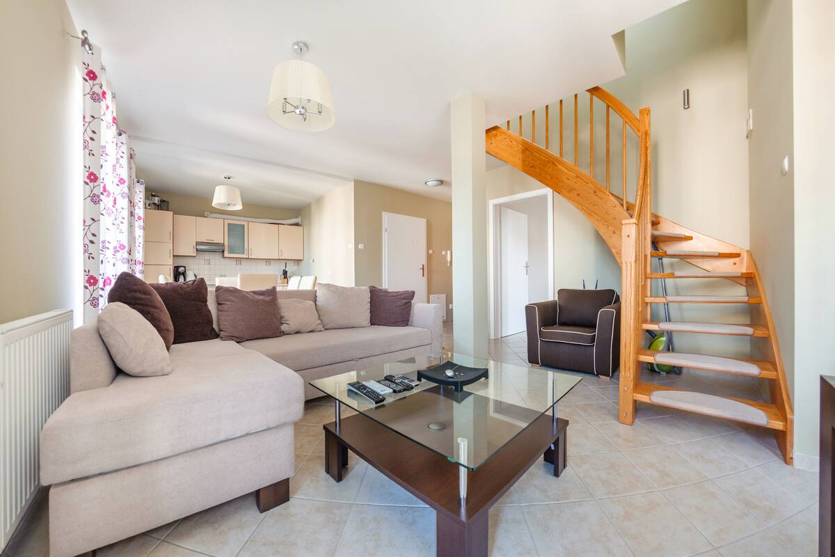 Un salon moderne avec une table basse en verre, un canapé, un fauteuil et un escalier en bois.