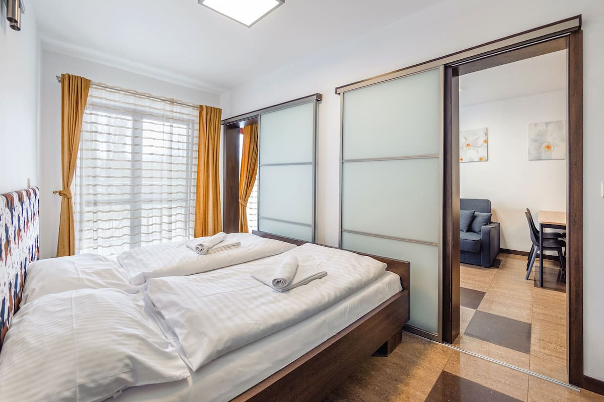 Une chambre d’hôtel avec deux lits, une grande fenêtre avec des rideaux, une porte coulissante donnant sur un coin repas et un design moderne.