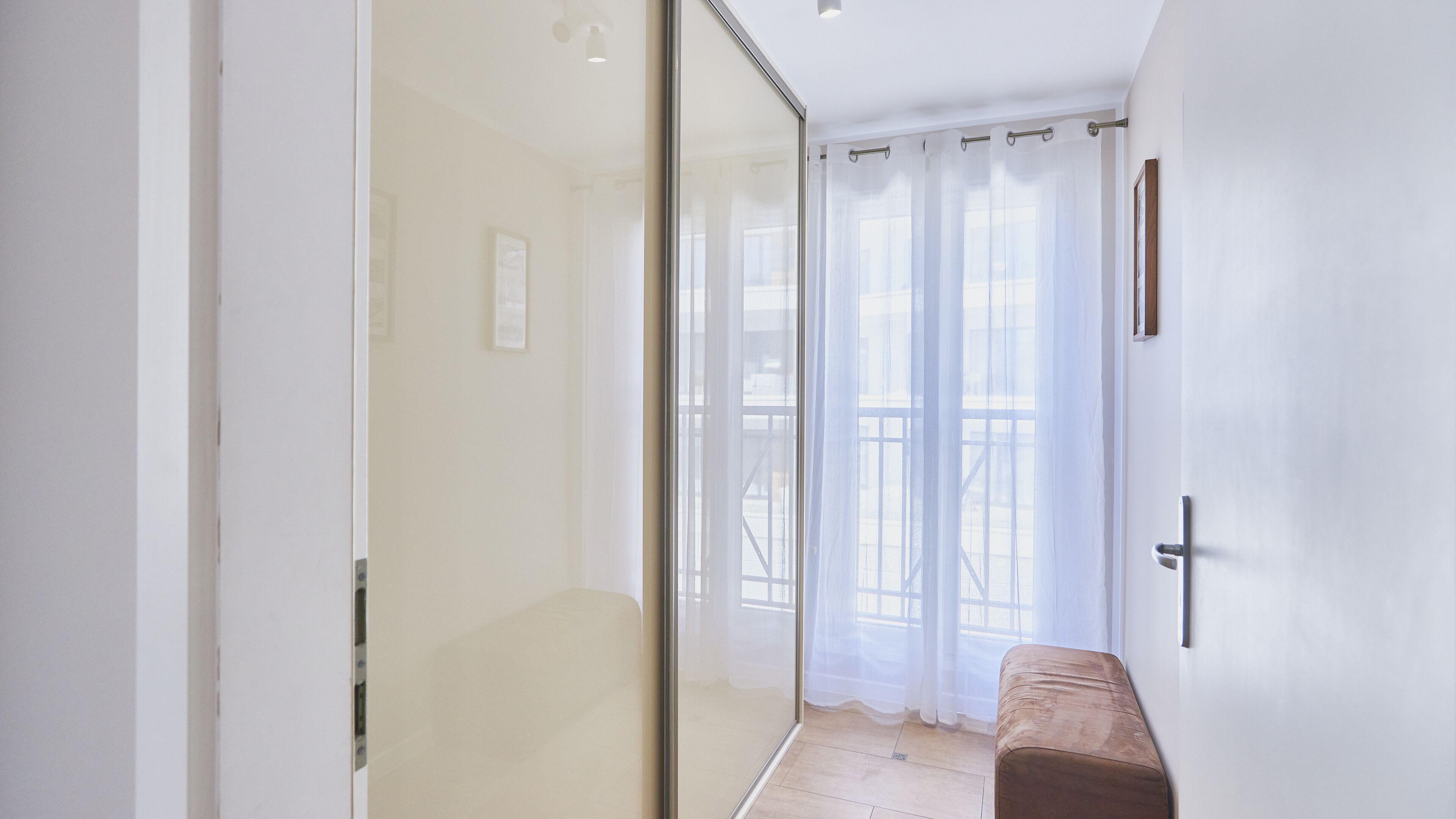 A modern bathroom with a glass shower enclosure, a bench, and a view of the outside balcony.