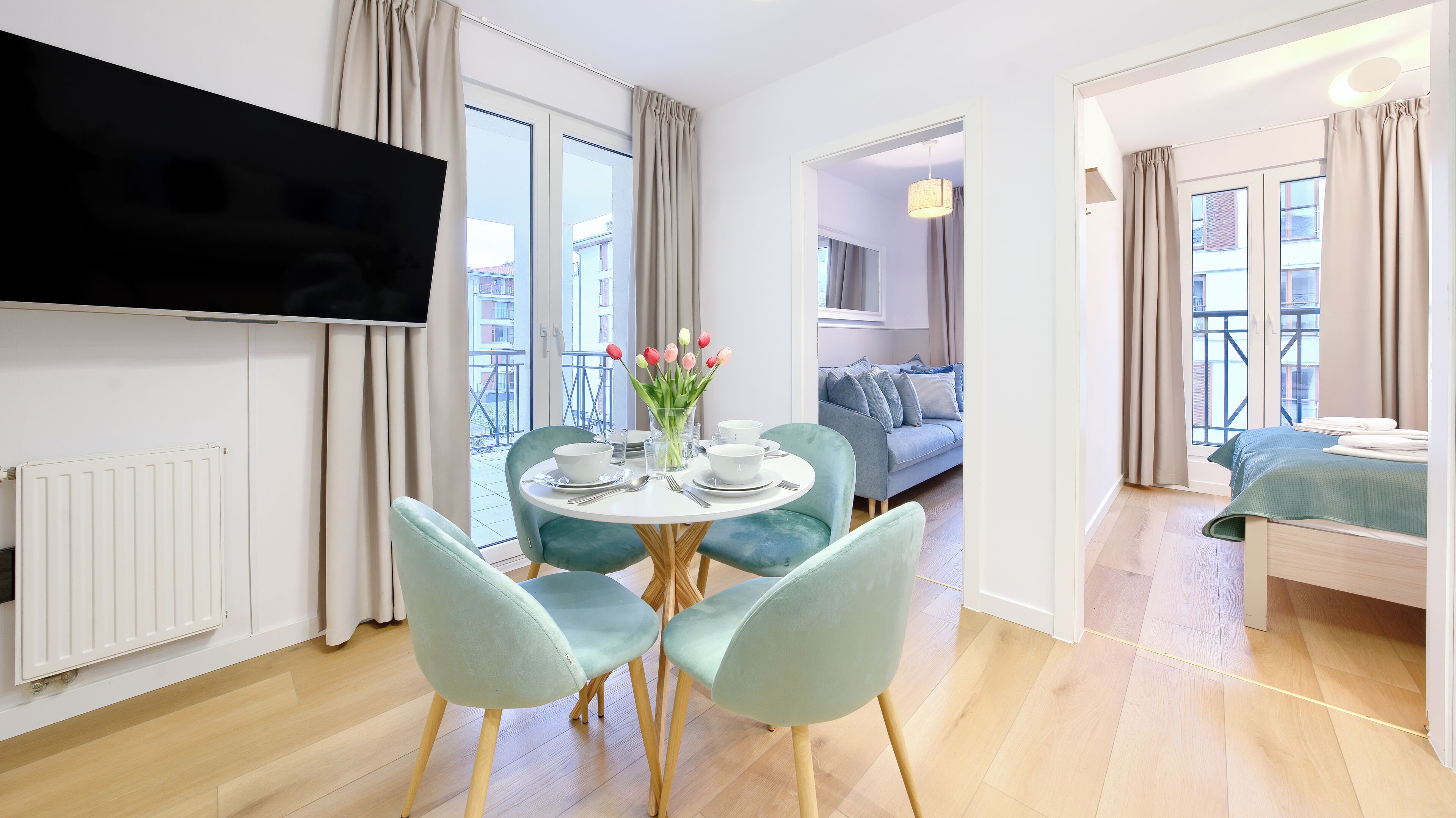 Ein modernes Hotelzimmer mit Essbereich, einem an der Wand befestigten Fernseher und einem Balkon mit Blick auf die Stadt.