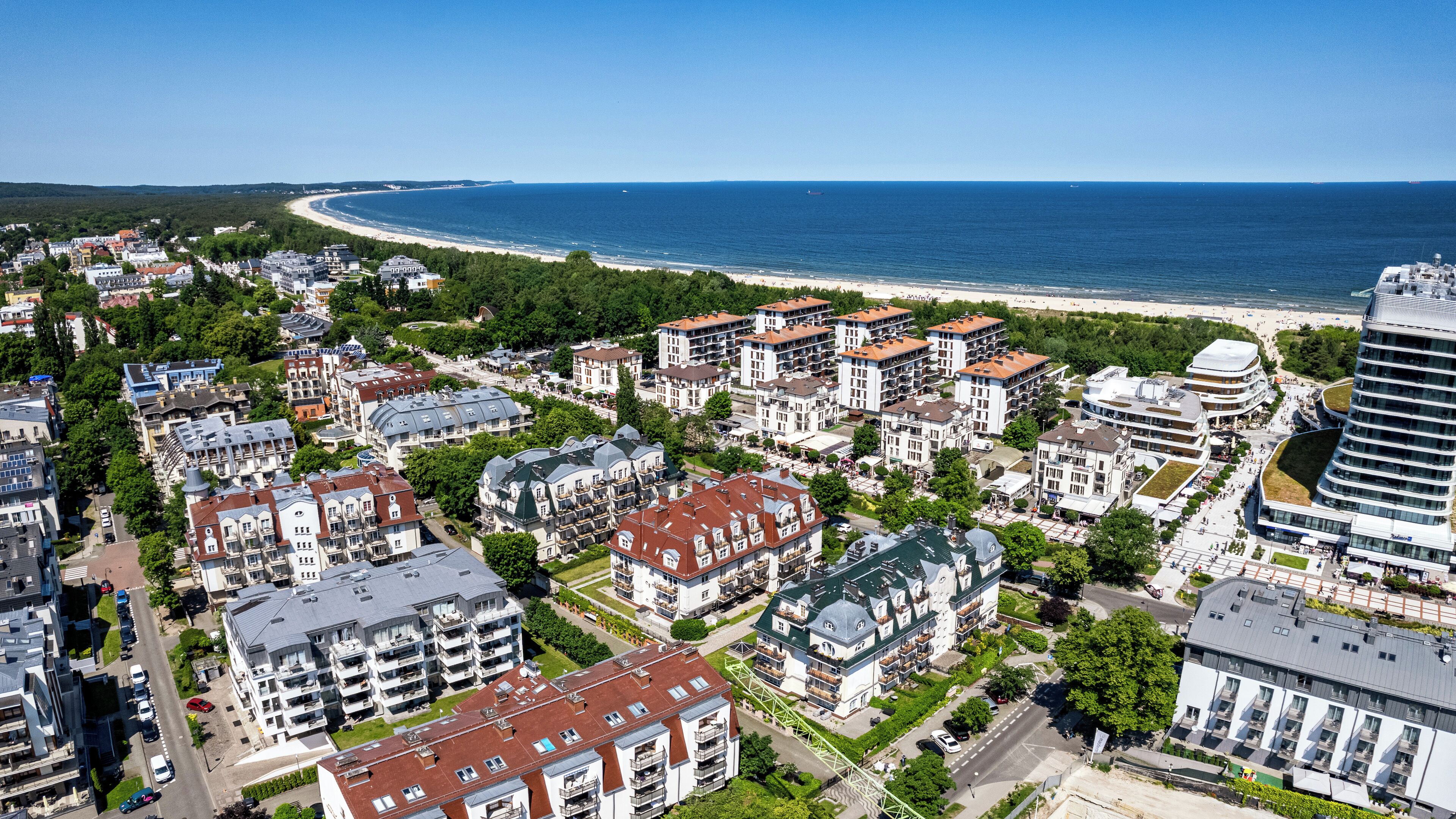 Vista aérea de un pueblo costero con playa, edificios residenciales y un hotel moderno.