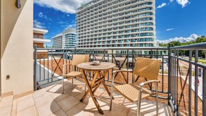 A balcony with wicker chairs and a table, overlooking a hotel with a modern design and a clear blue sky. - Apartamenty Sun & Snow Promenada (Swinoujscie)
