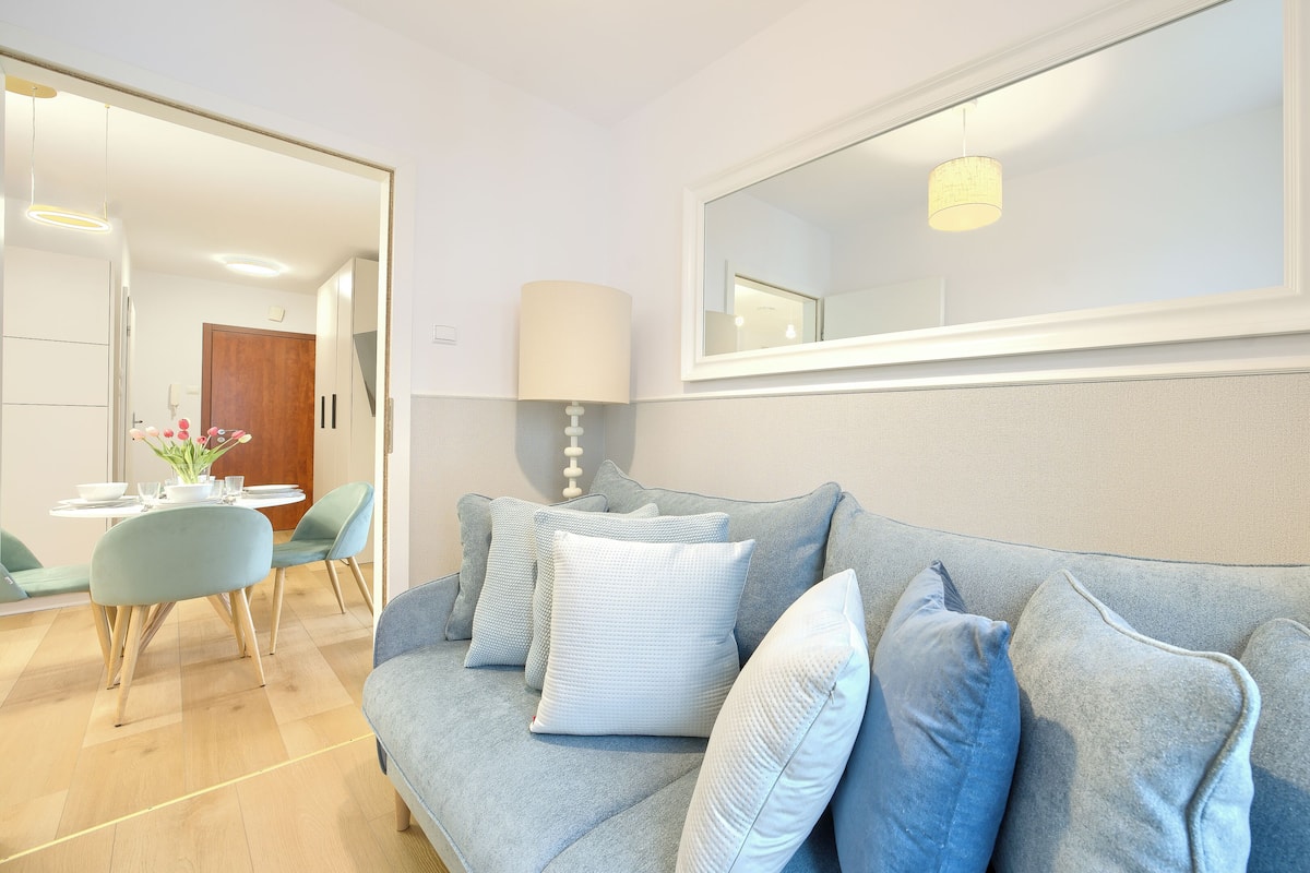 Un salon moderne avec un canapé gris, une table à manger avec des chaises et un grand miroir au mur.