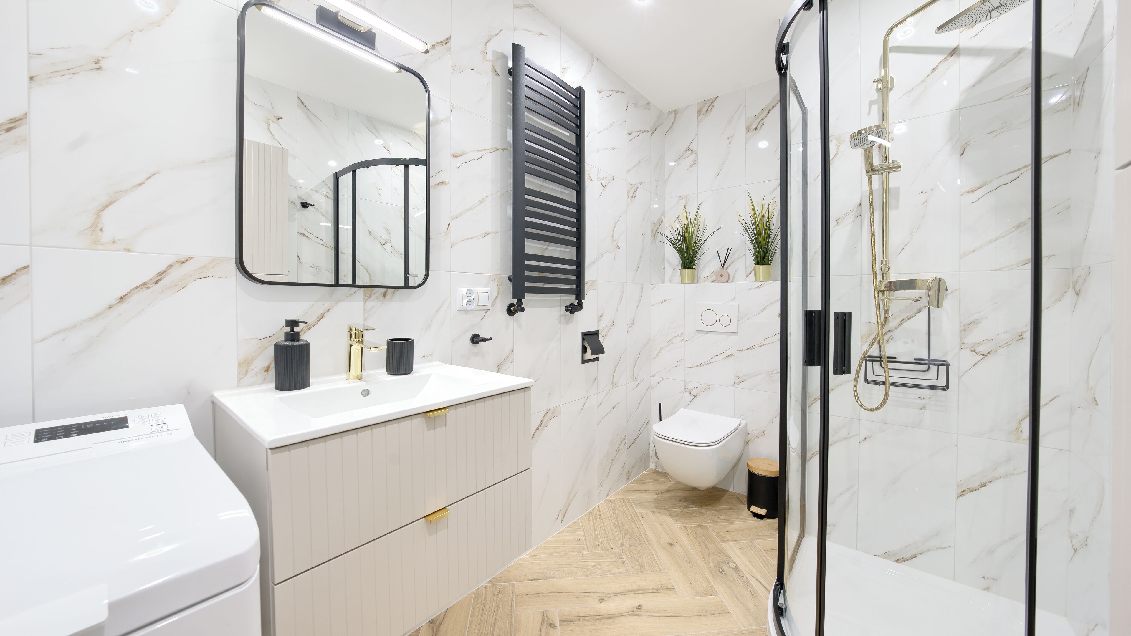 Un baño moderno con salpicadero de mármol, un espejo grande, inodoro empotrado, cabina de ducha y tocador con lavabo y toallero.