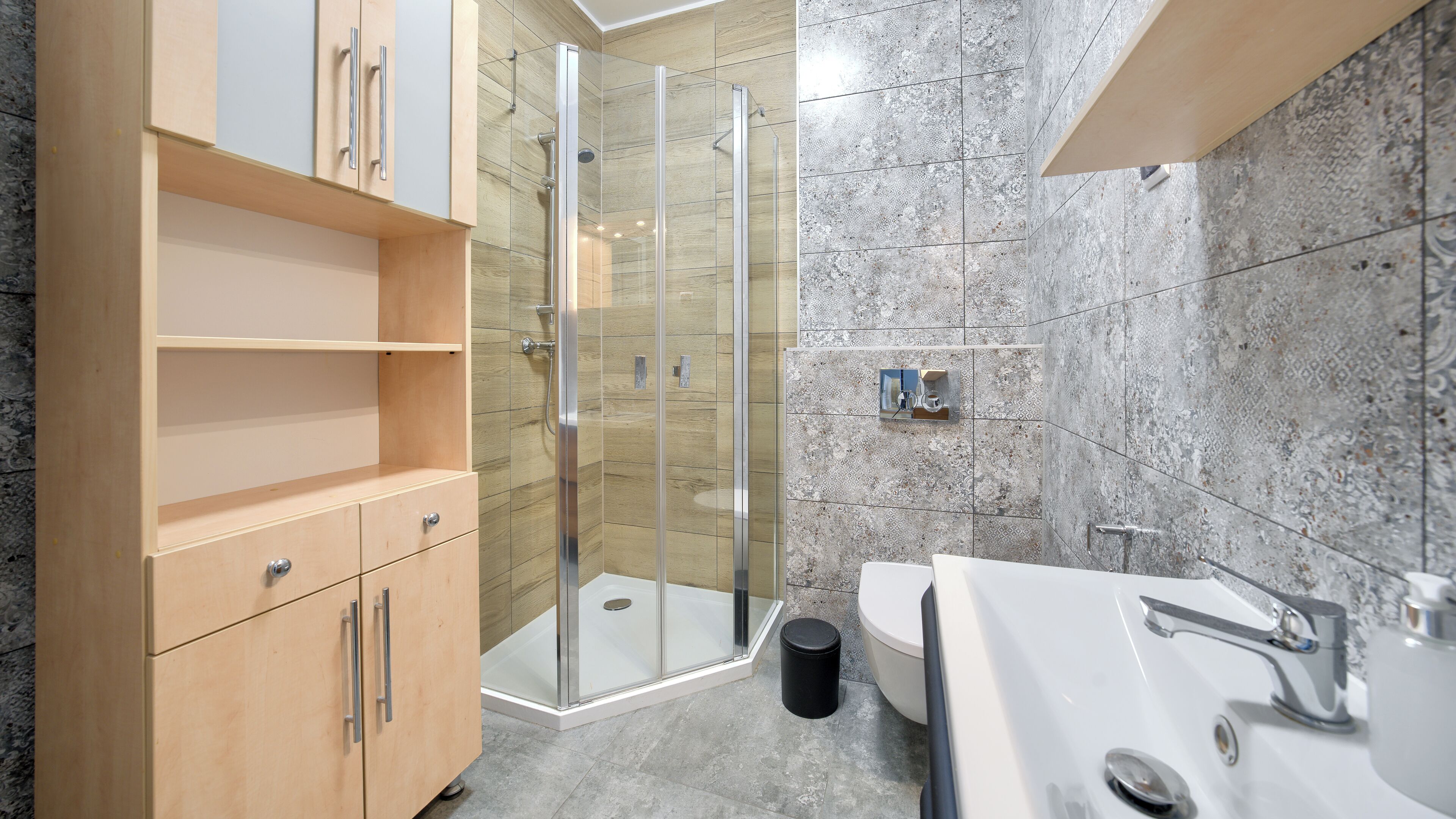 A modern bathroom with a glass-enclosed shower, wooden cabinets, and a marble-tiled wall.