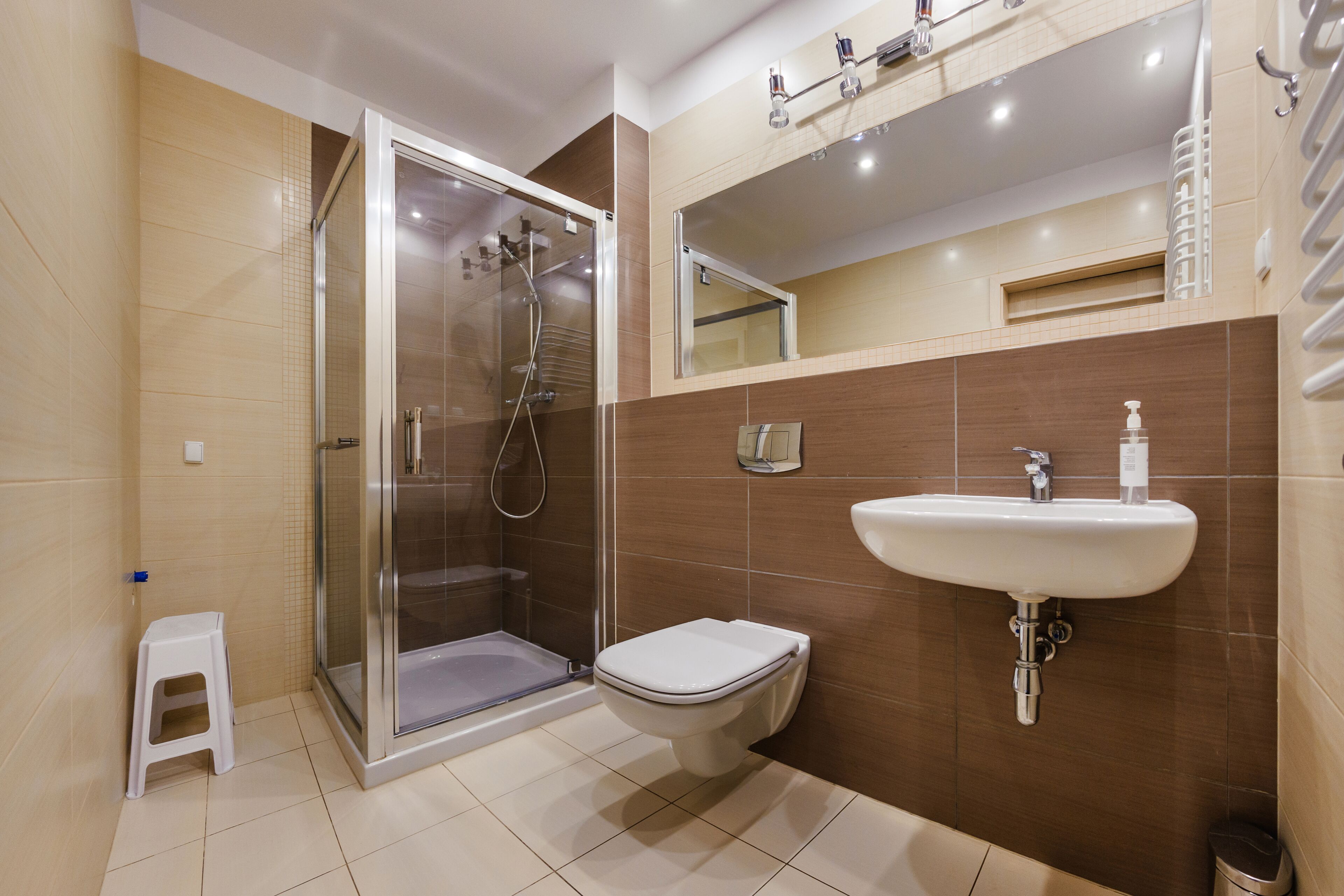 Un bany modern amb plat de dutxa envoltat de vidre, un vàter blanc i un lavabo fixat a la paret.