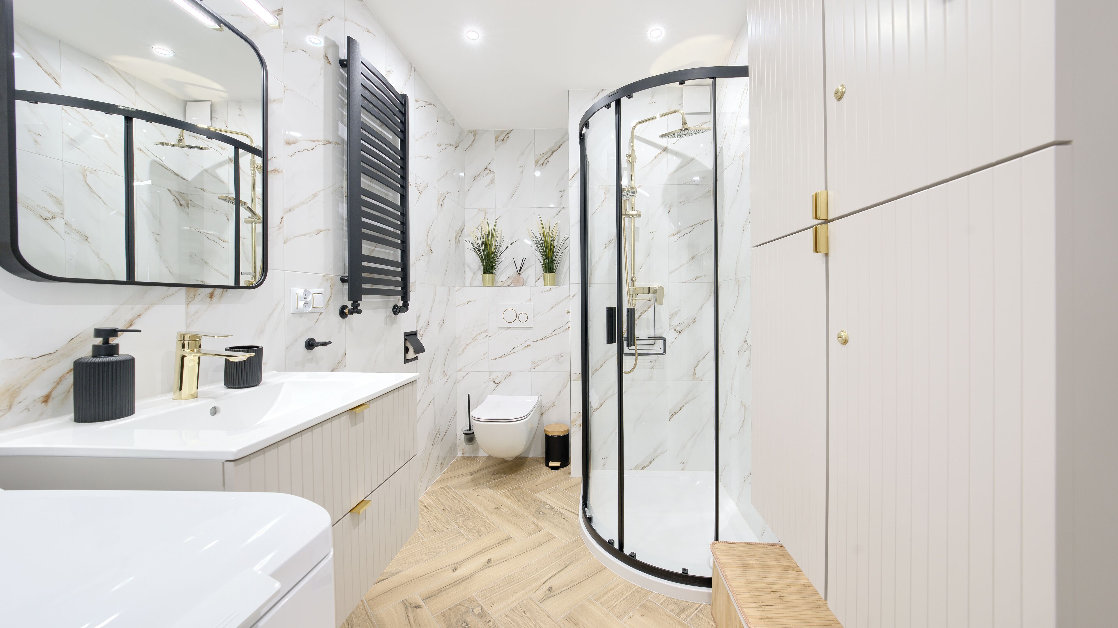 Ein modernes Badezimmer mit weißer Marmor-Spritzschutzwand, einem schwarzen Handtuchhalter, einer Duschkabine aus Glas und einem Holzboden.