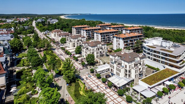 An aerial view of a coastal residential area with modern apartment buildings, a central pedestrian plaza, and a beach in the background. - Apartamenty Sun & Snow Promenada (Swinoujscie)