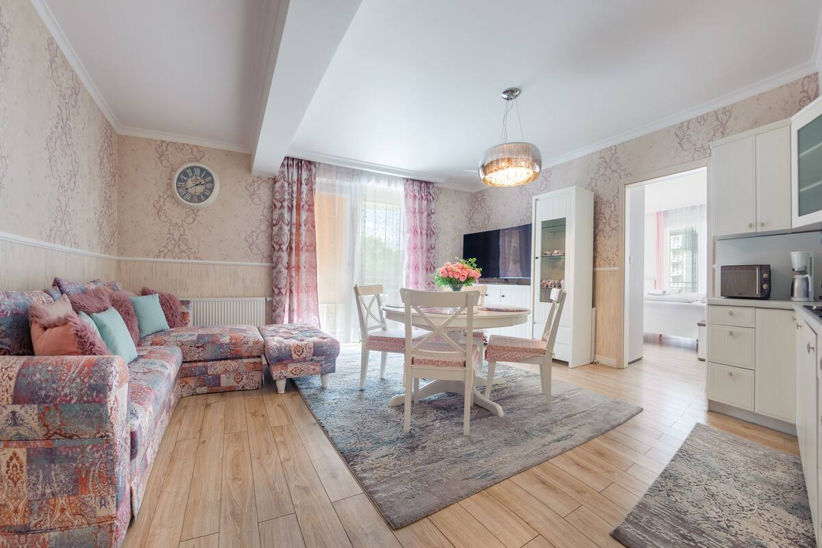 Un salon chaleureux avec un canapé, une table à manger et des chaises, et un coin cuisine visible à travers une porte ouverte.