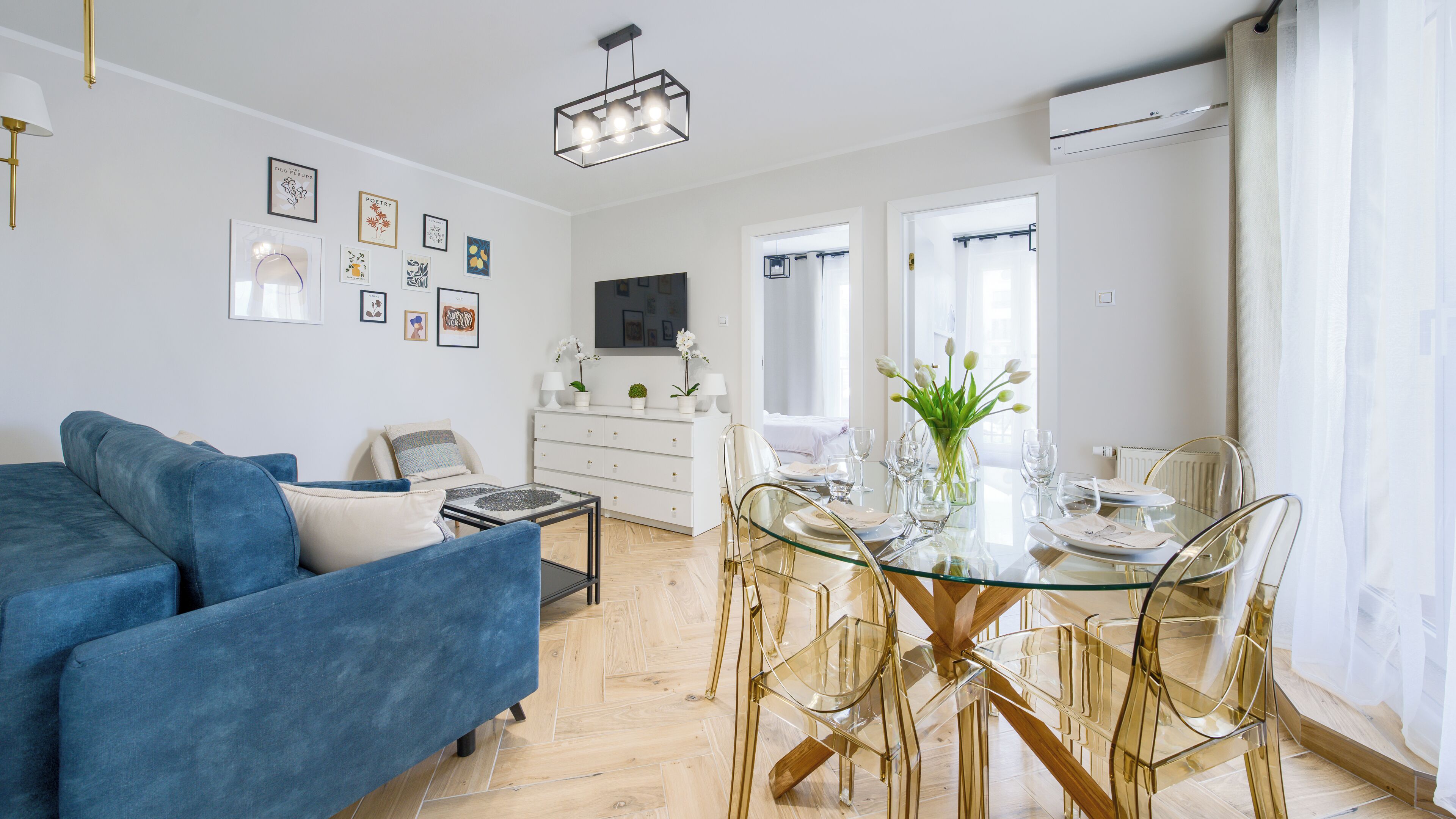 A modern living room with a blue sofa, a glass dining table with chairs, and a white dresser.