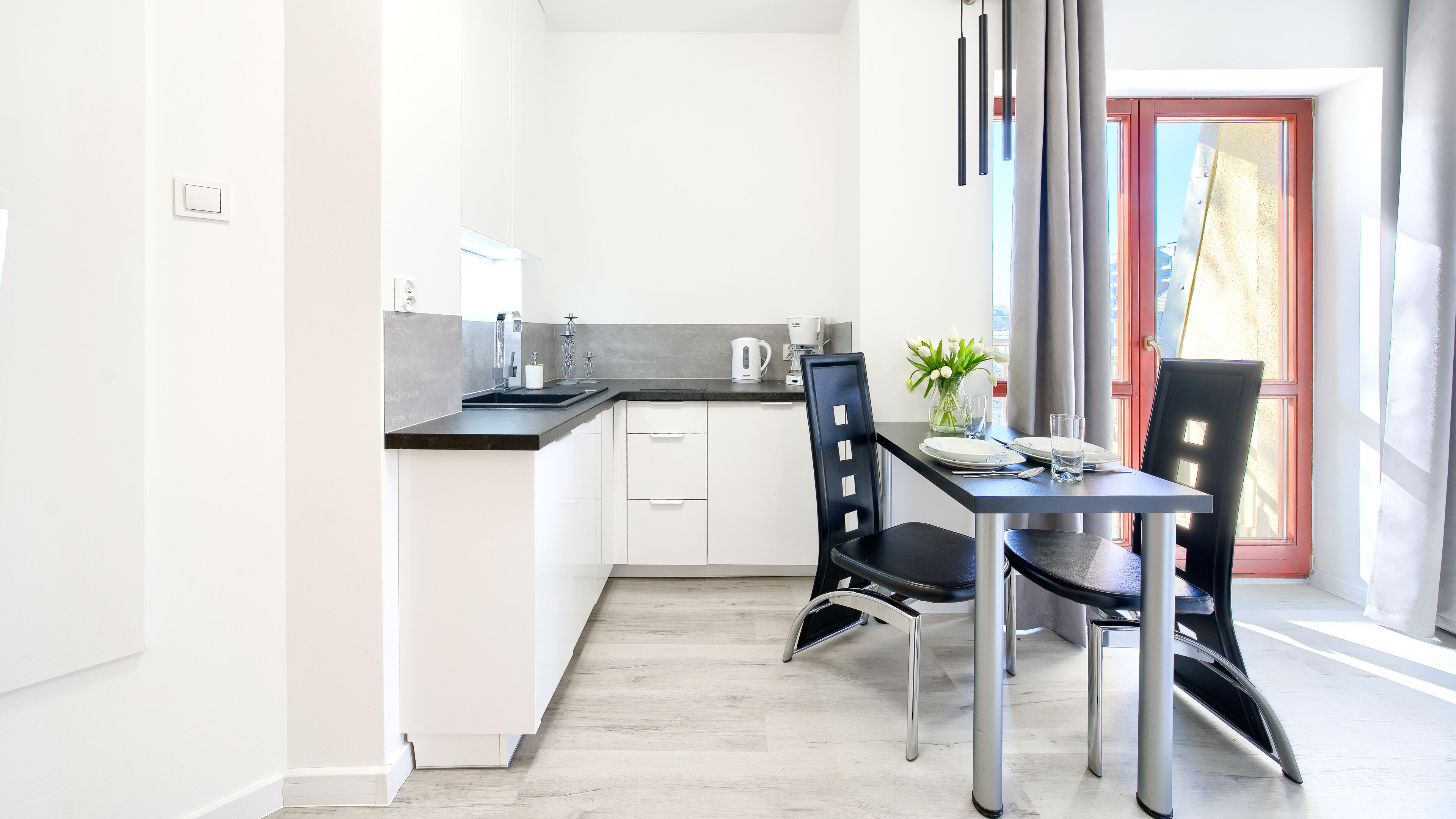 A modern kitchen with white cabinets, a black countertop, and a dining area with a table set for two.