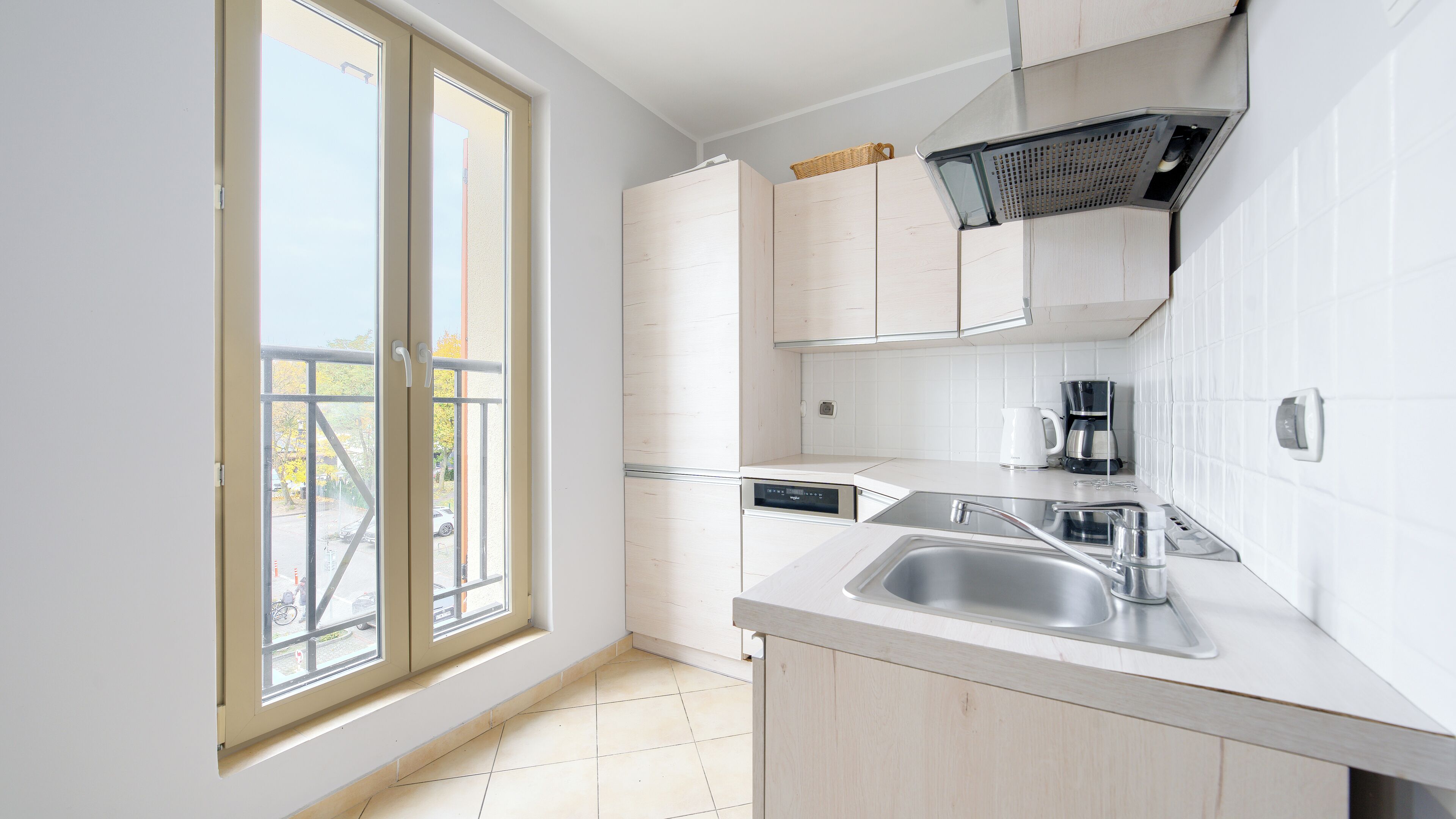 A modern kitchen with a large window, white cabinetry, and a stainless steel sink.